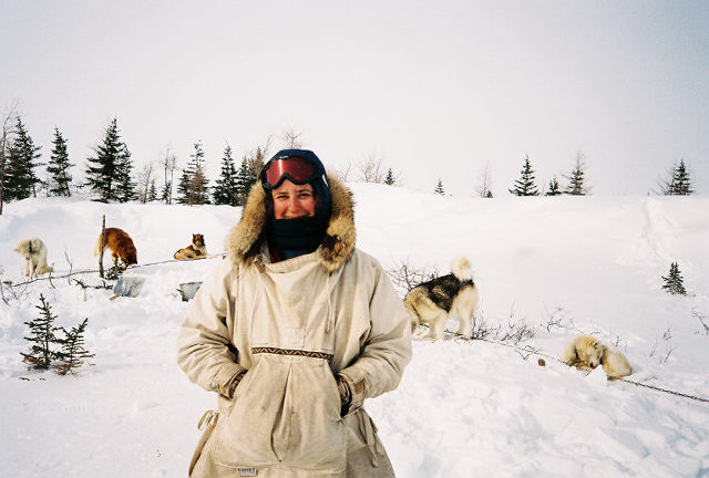 Iggy standing in the snow with sled dogs in the background